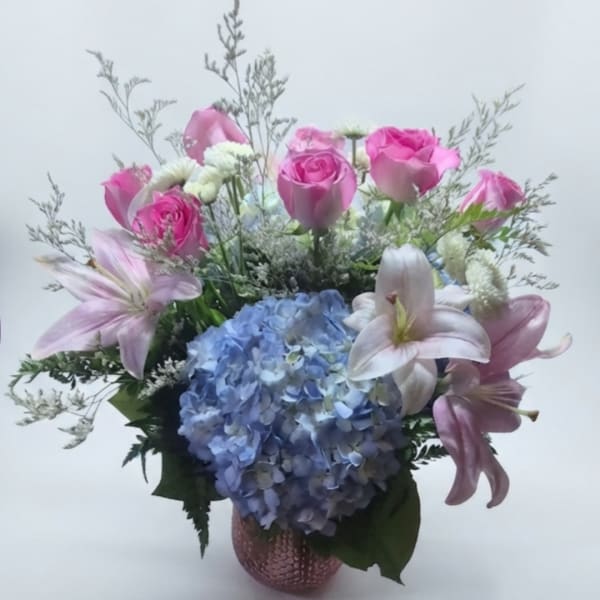 Pink roses and lilies arranged with a blue hydrangea in a pink vase