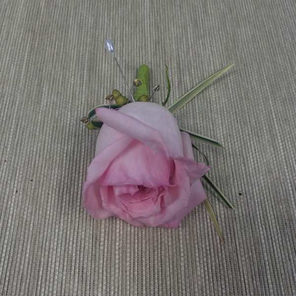 Pink rose boutonniere with decorative grass accents on a woven surface