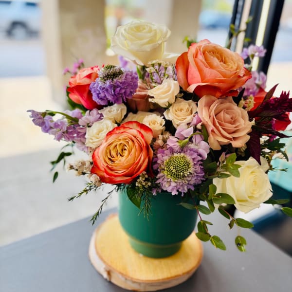 Mixed bouquet of roses and purple flowers in a green vase