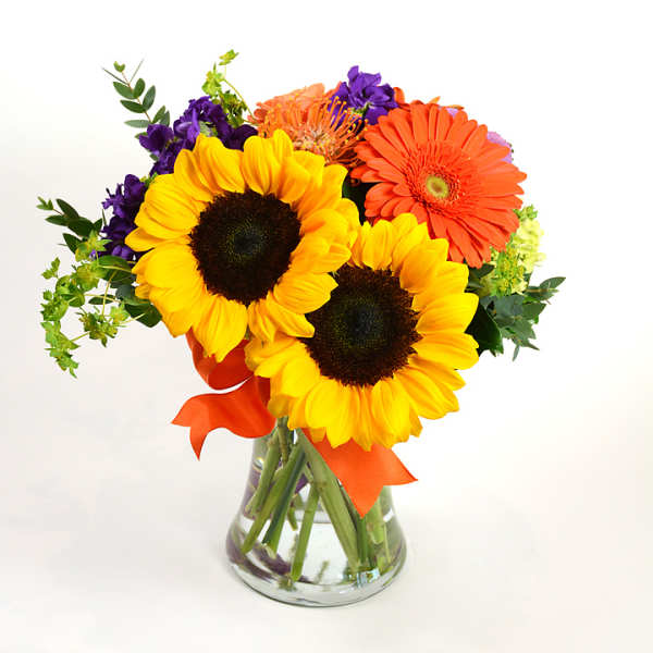 Bouquet of sunflowers, orange gerbera daisies, and purple flowers in a glass vase