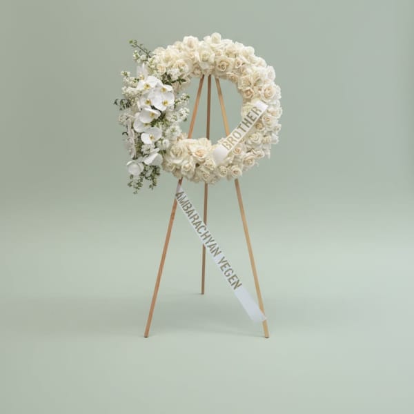 White floral wreath on a wooden easel with condolence ribbons