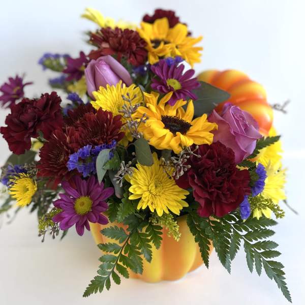 Mixed bouquet in a pumpkin-shaped container with yellow, purple, and burgundy flowers