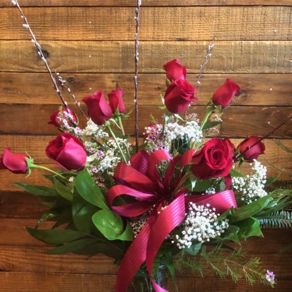 Red roses arranged in a glass vase with a pink ribbon