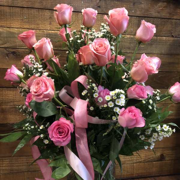 Pink roses and small white daisies in a glass vase with pink ribbon