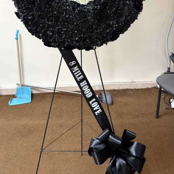 Large black floral wreath with a blue-and-white center on a stand