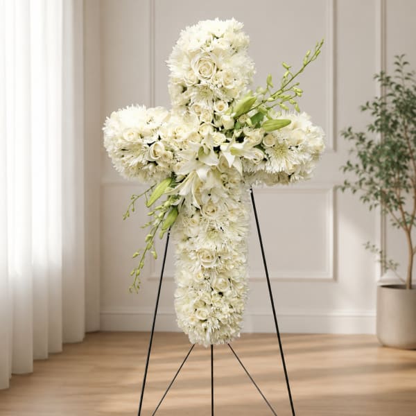 White floral cross arrangement on a stand with lilies and roses