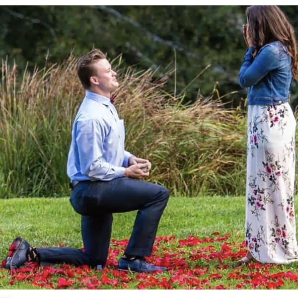 Man kneeling before woman standing on a flower petal-covered lawn