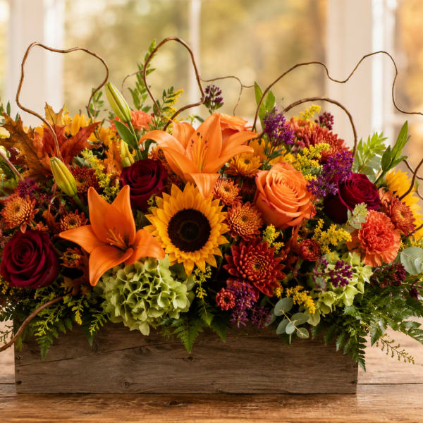 Autumn floral arrangement in a wooden box with lilies, roses, sunflowers, and mums