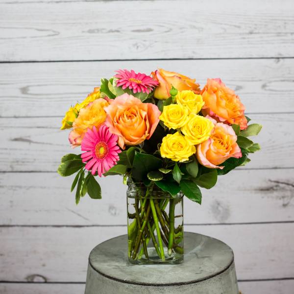 Bouquet of orange and yellow roses with pink gerbera daisies in a glass vase