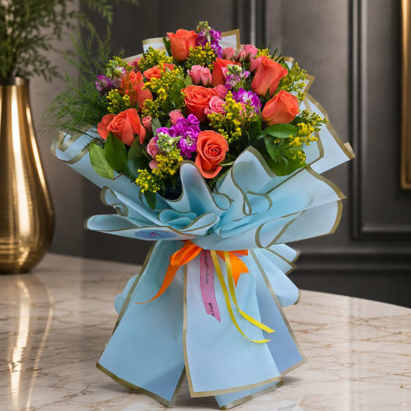 Bouquet of coral and pink roses with purple accents wrapped in blue paper