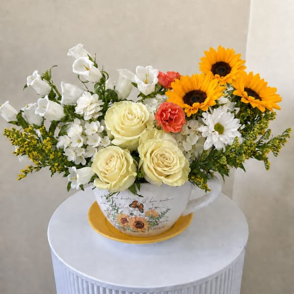 Mixed bouquet in a teacup vase with yellow roses, sunflowers, and white blooms
