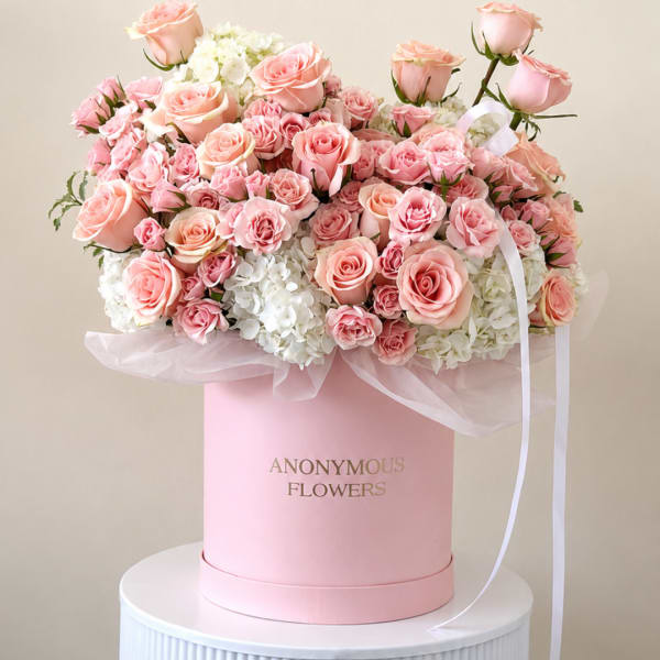 Pink roses and white hydrangeas arranged in a pink hat box with ribbon.