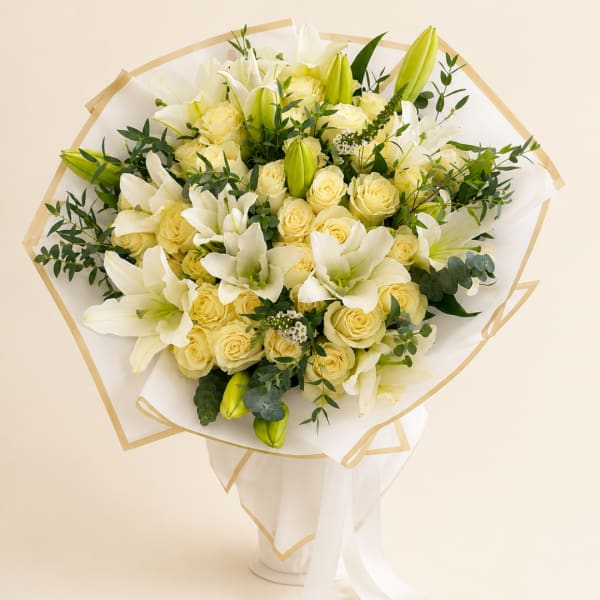 Bouquet of white lilies and pale yellow roses wrapped in white paper