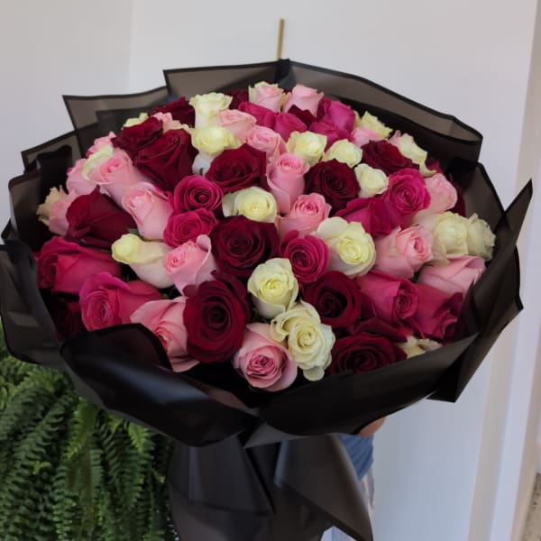 Bouquet of pink, red, and cream roses wrapped in black paper