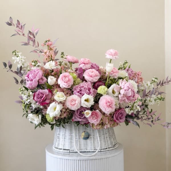 Pink and white floral arrangement in a white wicker basket