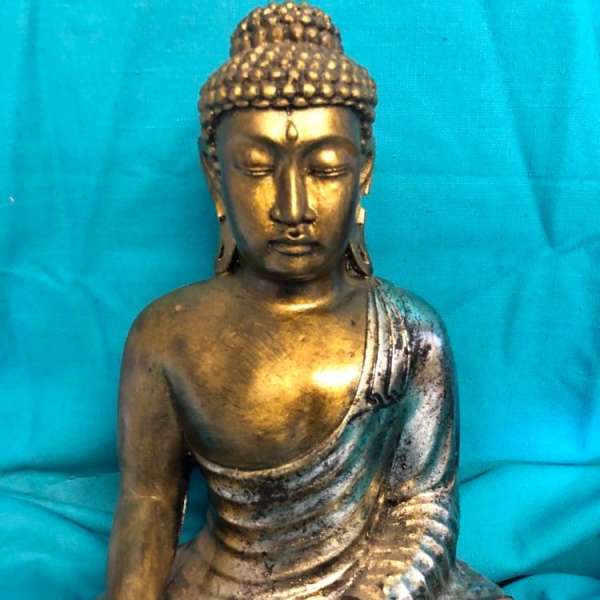 Gold Buddha statue seated against a blue fabric background