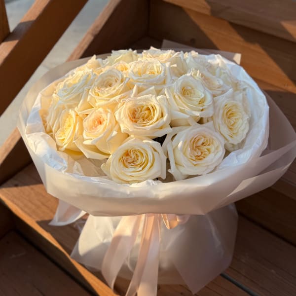 Bouquet of cream white roses wrapped in white paper with a ribbon