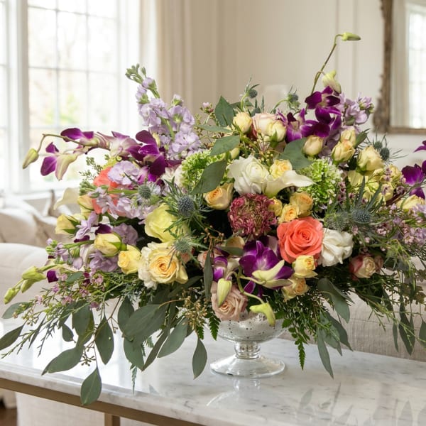 Mixed bouquet of roses, orchids, and lavender flowers in a glass vase