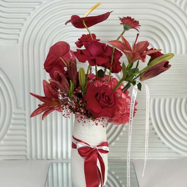 Red floral arrangement in a white vase with a ribbon bow