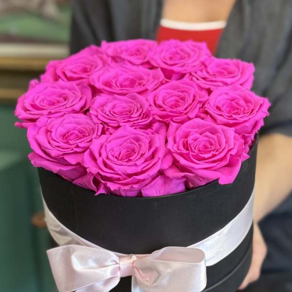 Bright pink roses arranged in a black round box with a pale ribbon bow