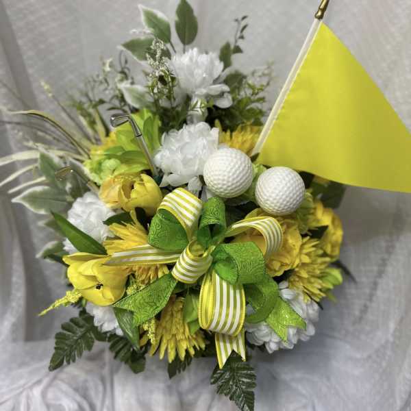 Yellow and white floral arrangement with golf balls and a small flag