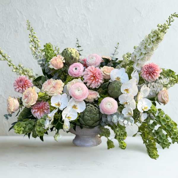 Low floral arrangement with pink blooms, white orchids, and green accents in a gray vase