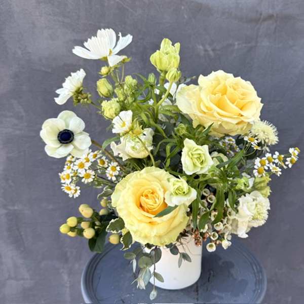 Yellow roses and white flowers arranged in a white vase