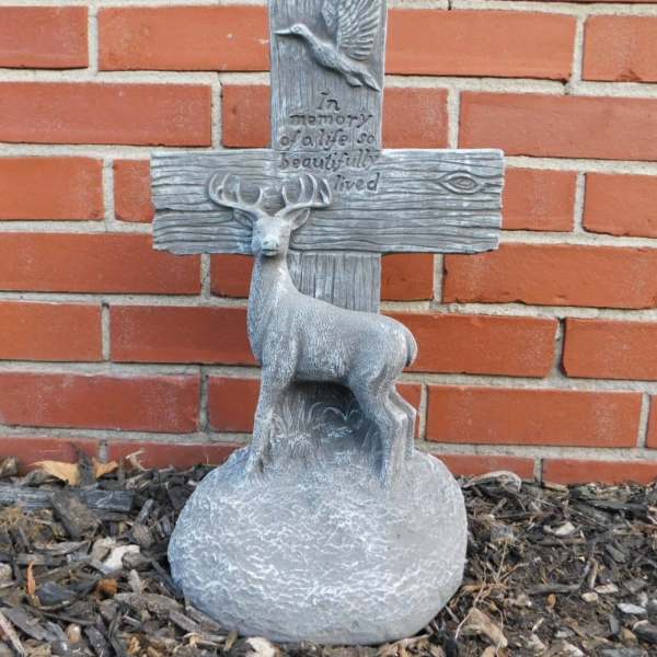 Gray memorial cross with a deer and bird relief against a brick wall