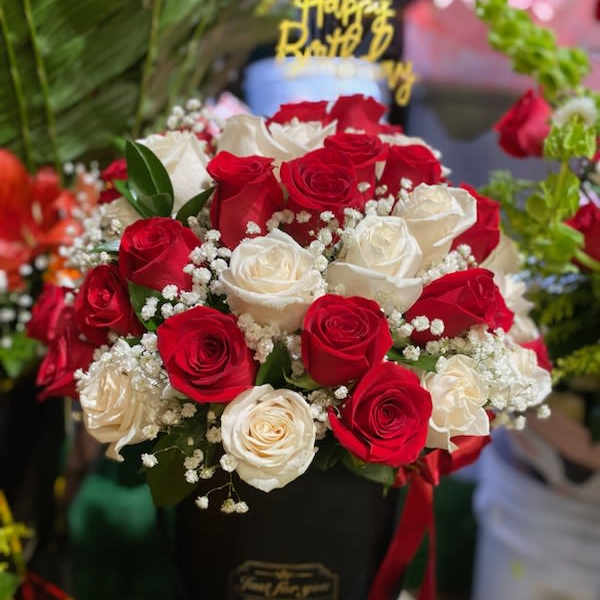 Red and white roses arranged in a black hatbox with a birthday topper