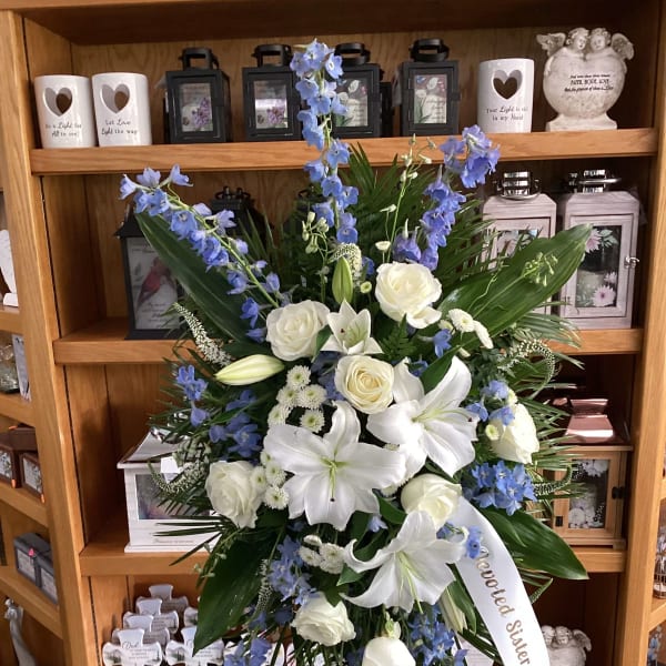 Standing sympathy spray with white lilies, roses, and blue flowers on an easel