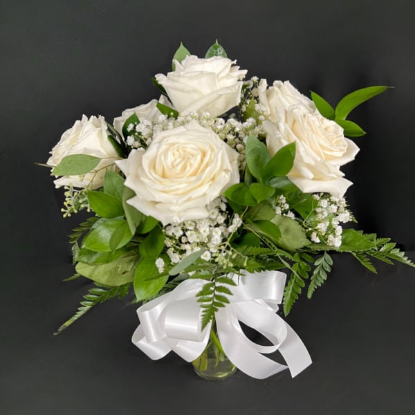 White roses in a glass vase with baby's breath and a white ribbon