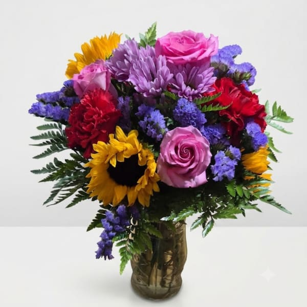 Mixed bouquet of roses, sunflowers, carnations, and purple blooms in a glass vase