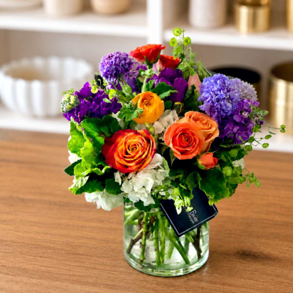 Mixed bouquet of roses, hydrangeas, and purple blooms in a glass vase