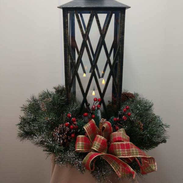 Black lantern centerpiece with candles, pine wreath, berries, and plaid ribbon
