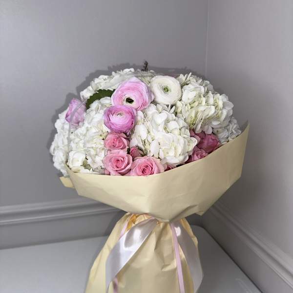 Bouquet of pink and white flowers wrapped in beige paper with ribbon