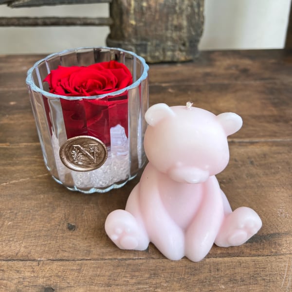 Red rose in a glass holder beside a pink bear-shaped candle