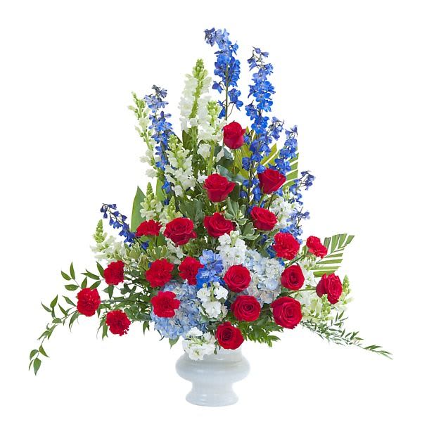 Tall red, white, and blue flower arrangement with roses and delphinium in a white pedestal vase
