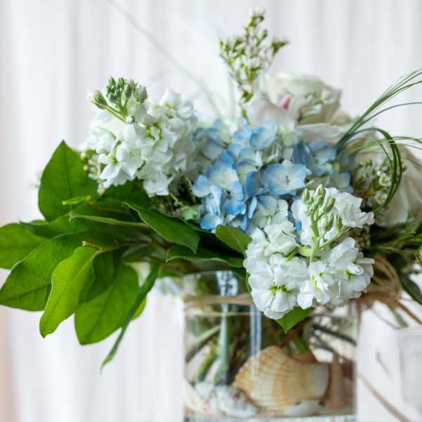 Blue and white flowers arranged in a glass vase with broad green leaves