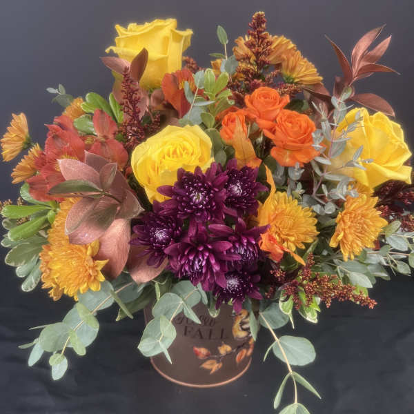 Fall bouquet with yellow roses, orange spray roses, and purple chrysanthemums in a decorative container