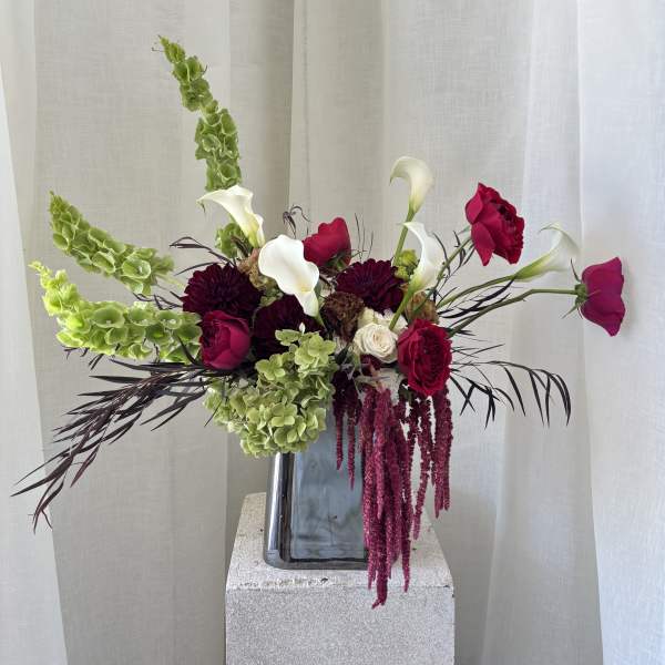 Tall floral arrangement with white calla lilies, magenta roses, and green hanging blooms in a vase.