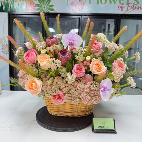 Basket arrangement of pink and peach roses with orchids and protea
