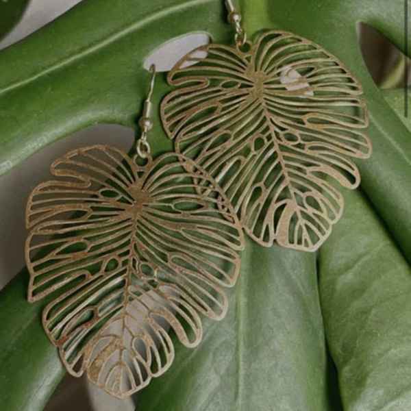 Pair of gold leaf-shaped dangle earrings on a green leaf background