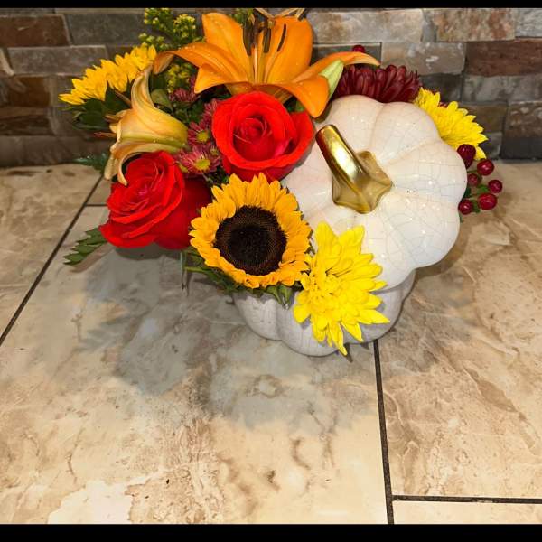 Floral arrangement in a white pumpkin container with red, yellow, and orange blooms
