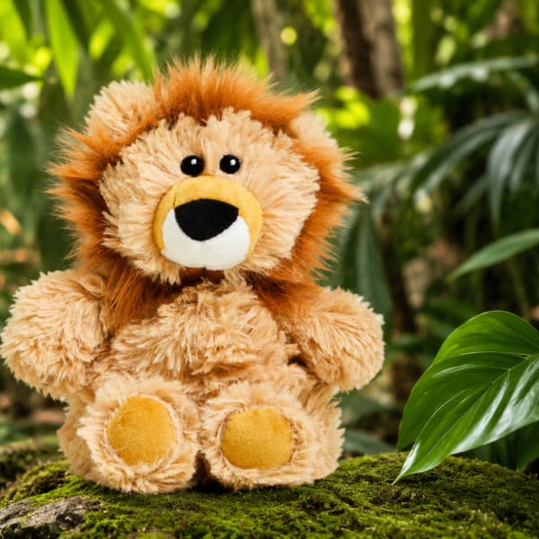 Plush lion sitting on moss with tropical plants in the background