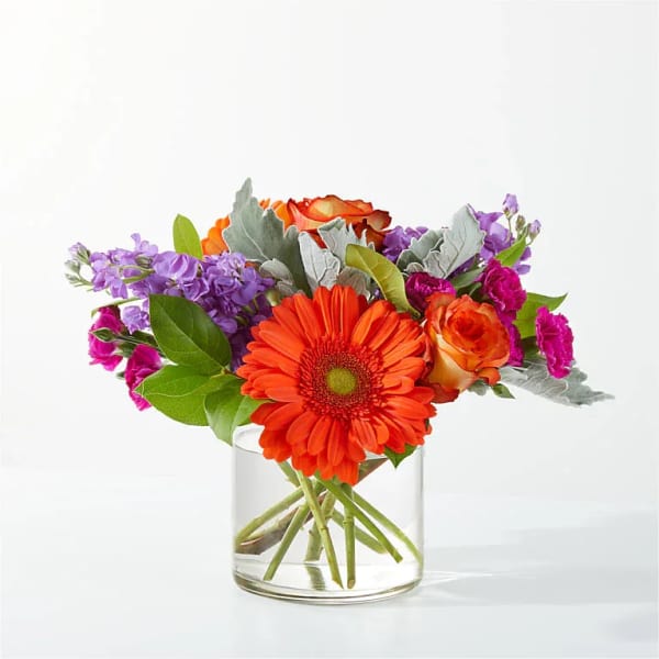 Orange gerbera bouquet in a clear glass vase with purple and pink flowers
