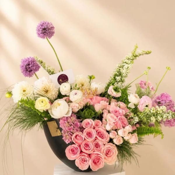 Pink and white rose arrangement in a black vase with purple blooms