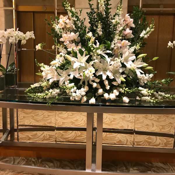 Large white floral arrangement with lilies and orchids on a table