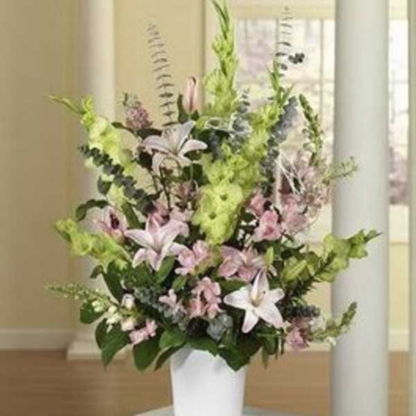 Tall floral arrangement in a white pot with pink lilies and greenery
