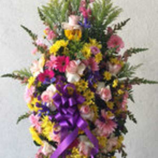 Tall standing floral spray with pink, yellow, and purple flowers and a purple ribbon