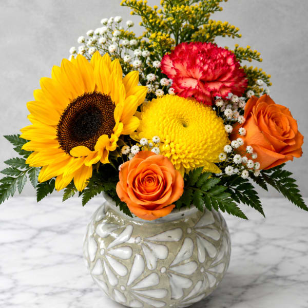 Mixed bouquet with a sunflower, roses, and carnations in a decorative vase
